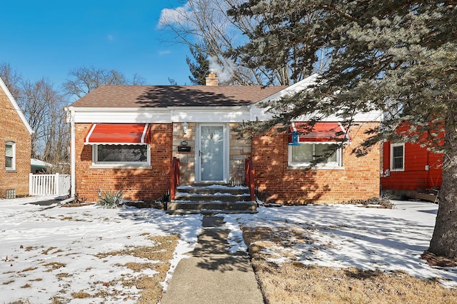 bungalow-style home featuring a shingled roof, fence, brick siding, and a chimney