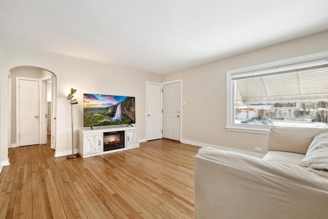 unfurnished living room featuring a glass covered fireplace, light wood-style flooring, baseboards, and arched walkways