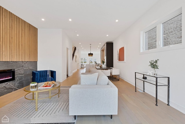 living room with a glass covered fireplace, recessed lighting, light wood-style flooring, and baseboards