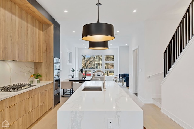 kitchen featuring tasteful backsplash, a sink, stainless steel gas stovetop, modern cabinets, and a kitchen island with sink