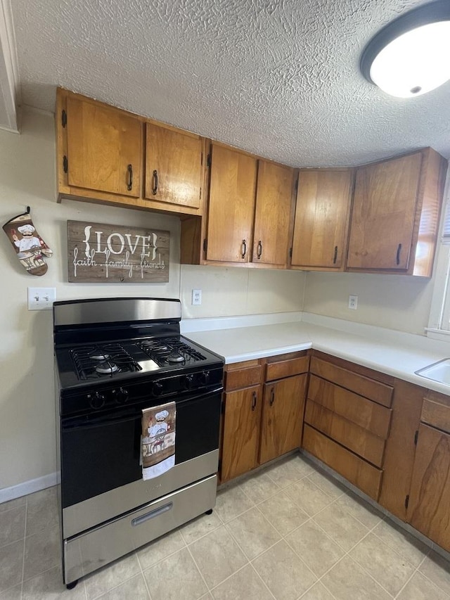 kitchen featuring brown cabinetry, stainless steel range with gas stovetop, light countertops, and a textured ceiling