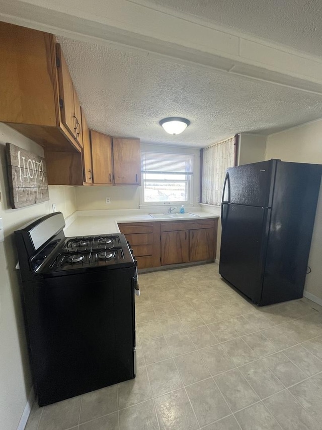 kitchen featuring a sink, range with gas stovetop, brown cabinets, and freestanding refrigerator