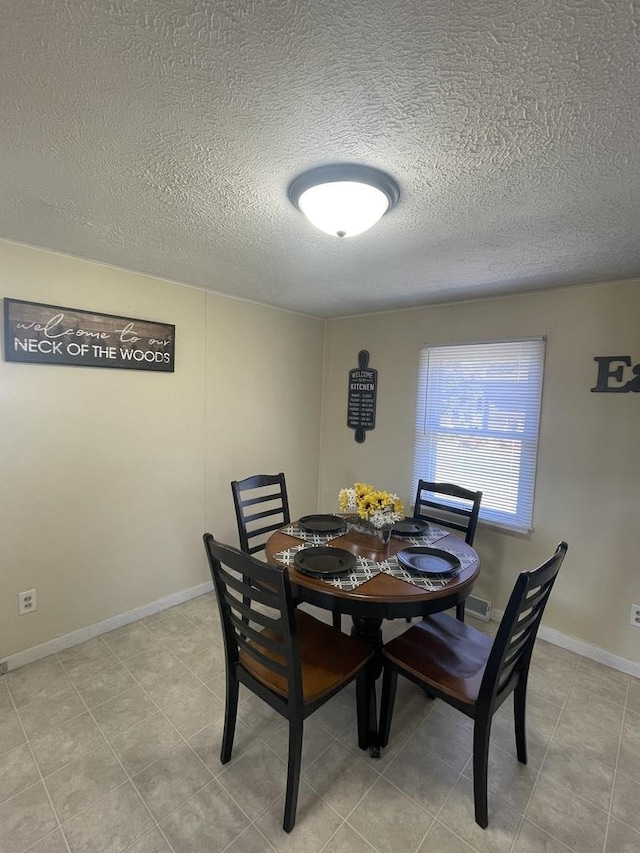 dining room featuring light tile patterned floors, baseboards, and a textured ceiling