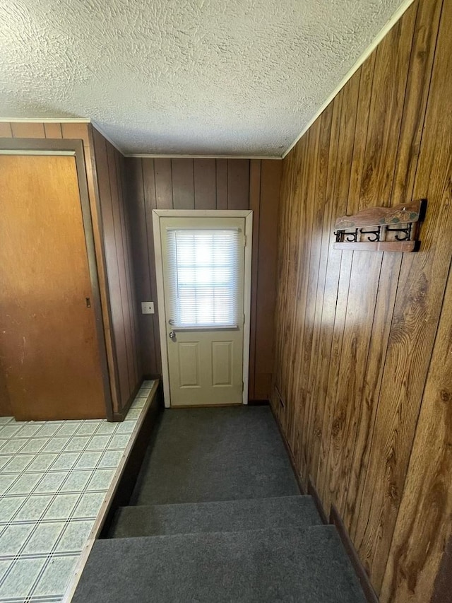 doorway to outside with wood walls, carpet floors, and a textured ceiling