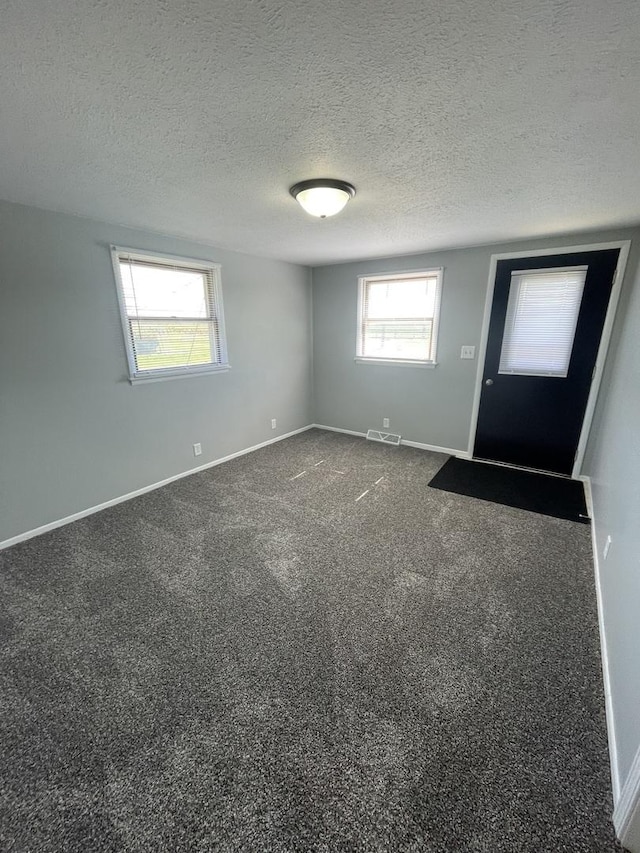 empty room featuring baseboards, visible vents, dark carpet, and a textured ceiling