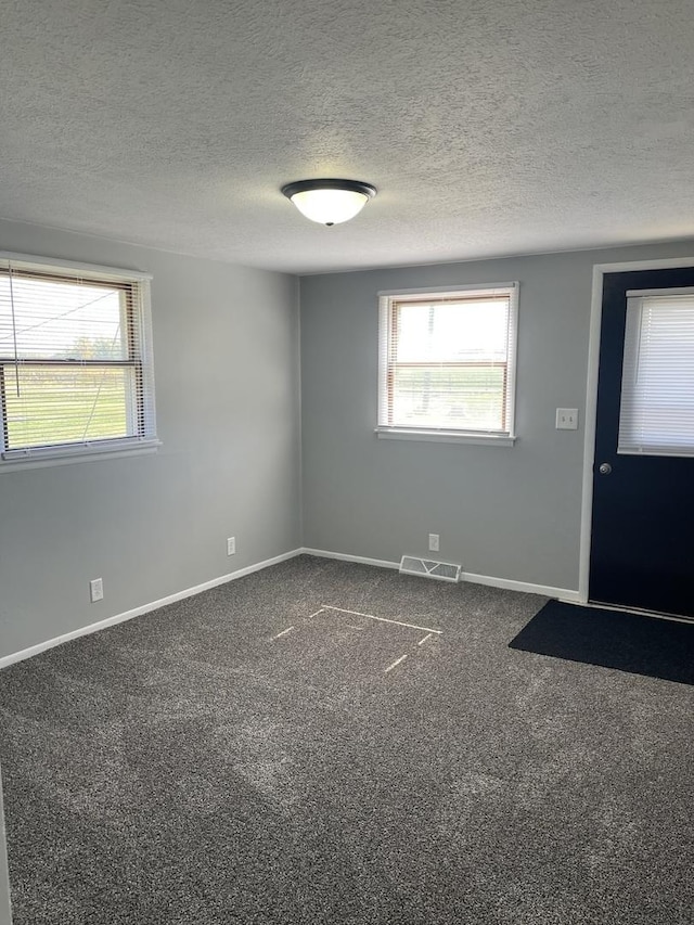 unfurnished room with dark colored carpet, visible vents, baseboards, and a textured ceiling