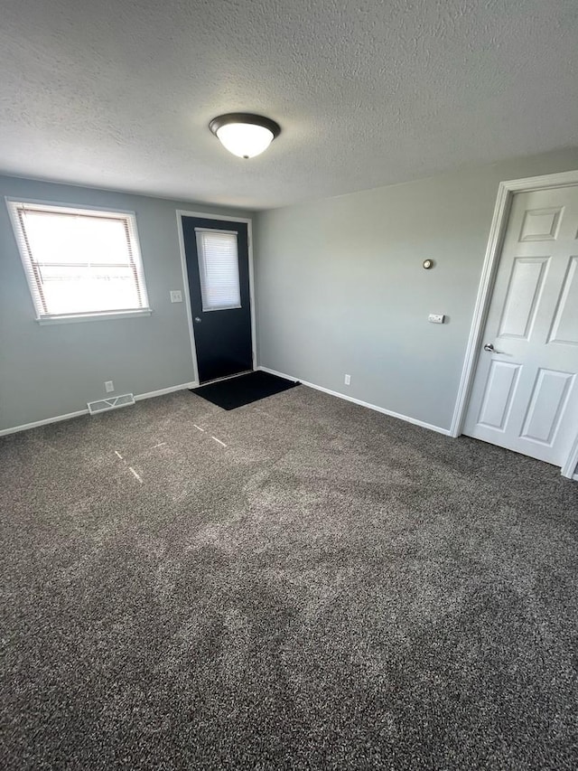 entryway featuring visible vents, baseboards, a textured ceiling, and dark carpet