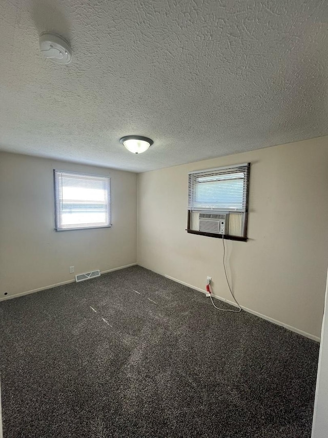 empty room with cooling unit, baseboards, visible vents, a textured ceiling, and dark colored carpet