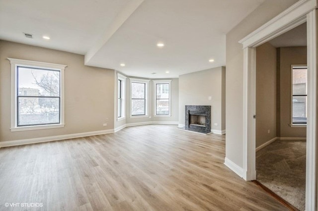 unfurnished living room featuring light wood-style floors, a fireplace, visible vents, and baseboards