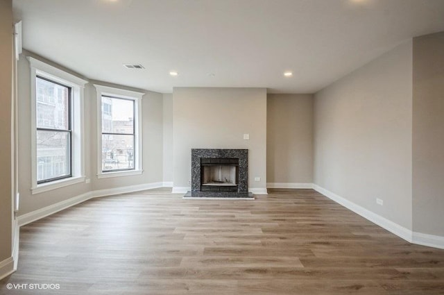 unfurnished living room with visible vents, wood finished floors, recessed lighting, a premium fireplace, and baseboards