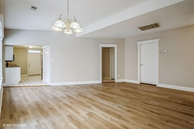 empty room featuring light wood-type flooring, visible vents, baseboards, and a notable chandelier