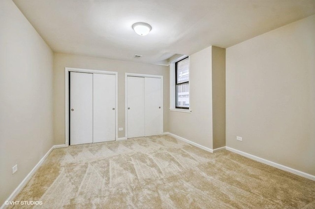 unfurnished bedroom featuring baseboards, multiple closets, and carpet flooring