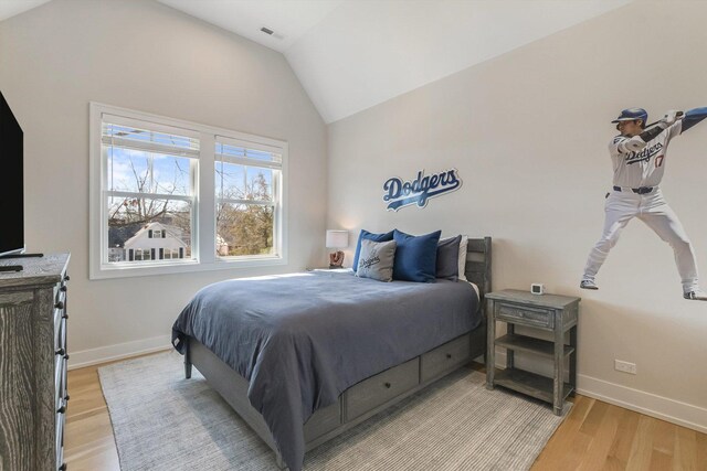 bedroom with visible vents, lofted ceiling, baseboards, and light wood finished floors