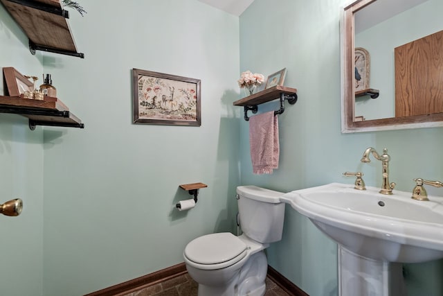 half bath with toilet, baseboards, and a sink