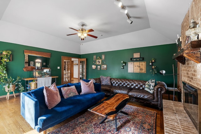 living area featuring wood finished floors, a ceiling fan, baseboards, lofted ceiling, and a brick fireplace