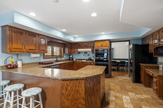 kitchen with under cabinet range hood, recessed lighting, a peninsula, black appliances, and a sink