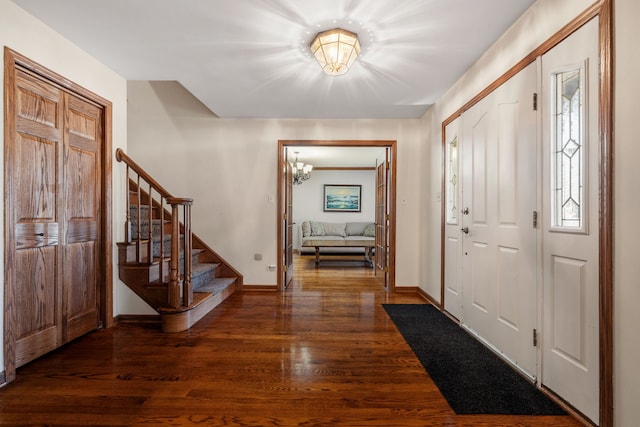 foyer with stairway, an inviting chandelier, dark wood-type flooring, and baseboards