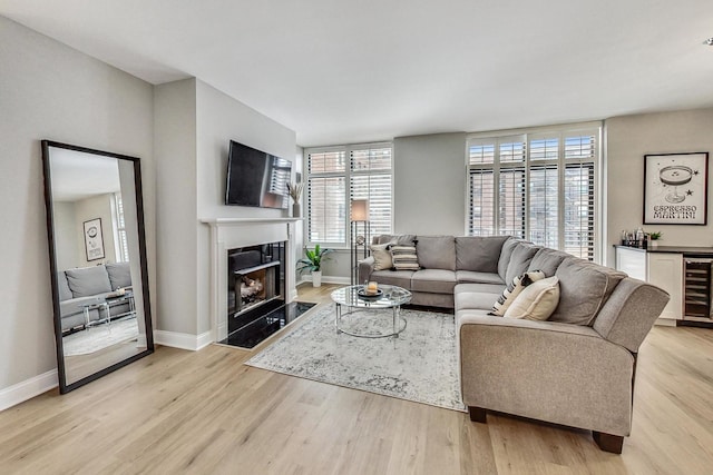 living room featuring wine cooler, a premium fireplace, baseboards, and light wood-style floors