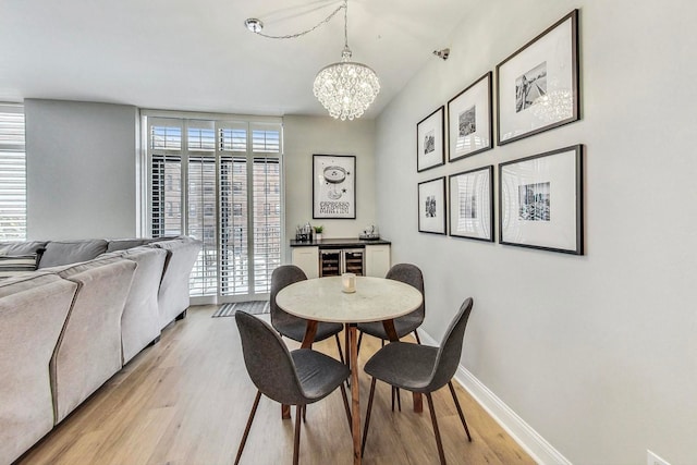 dining space with light wood-style floors, wine cooler, a notable chandelier, and plenty of natural light