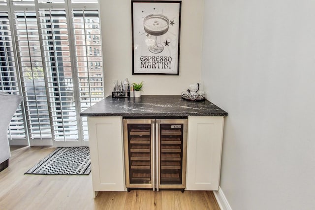 bar with wine cooler, light wood finished floors, baseboards, and a dry bar