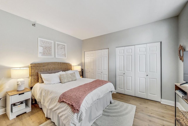 bedroom with baseboards, multiple closets, and light wood-style flooring