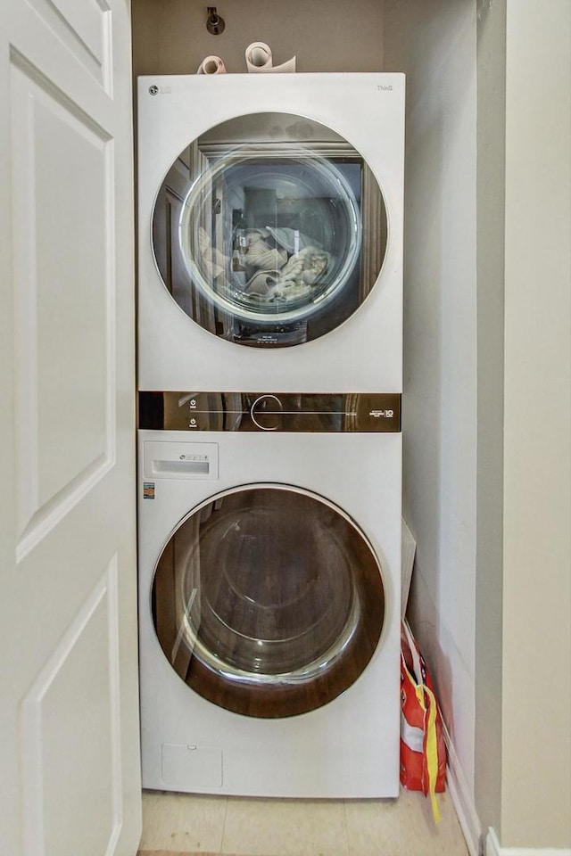 clothes washing area with tile patterned floors, stacked washer and dryer, and laundry area