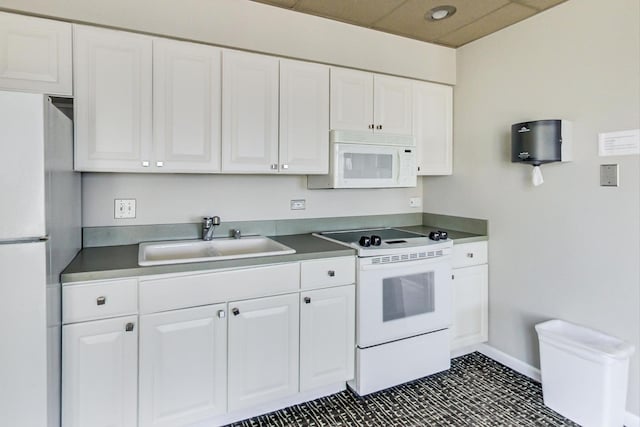 kitchen featuring dark countertops, baseboards, white appliances, white cabinetry, and a sink