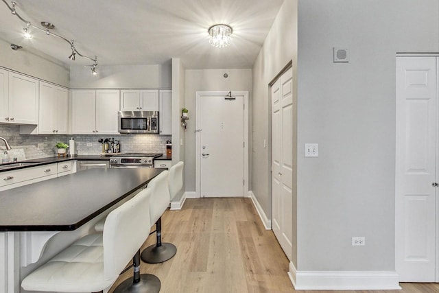 kitchen featuring dark countertops, decorative backsplash, appliances with stainless steel finishes, white cabinets, and a sink