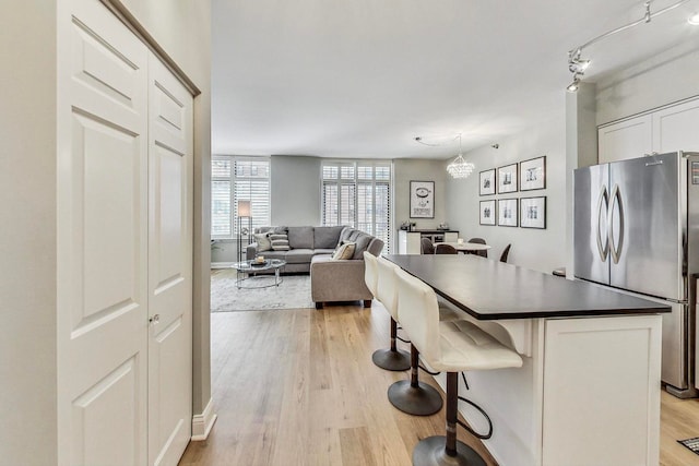 kitchen featuring light wood finished floors, a breakfast bar, freestanding refrigerator, white cabinets, and dark countertops