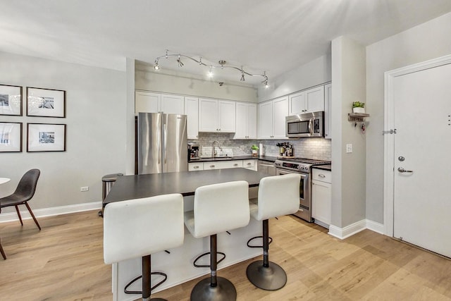 kitchen with a sink, decorative backsplash, stainless steel appliances, light wood-style floors, and dark countertops