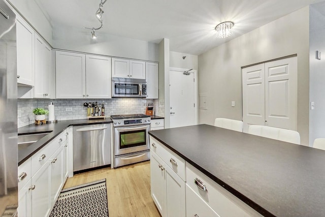 kitchen featuring dark countertops, light wood-style floors, appliances with stainless steel finishes, white cabinets, and decorative backsplash