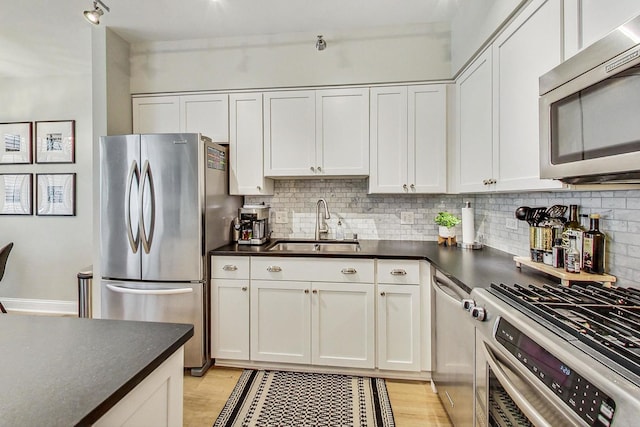 kitchen featuring dark countertops, tasteful backsplash, white cabinets, stainless steel appliances, and a sink