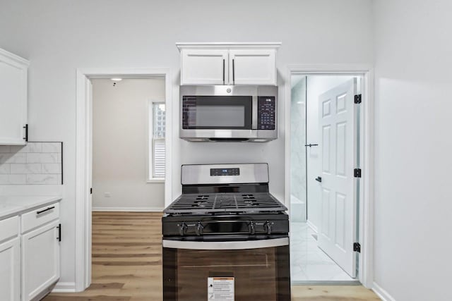 kitchen featuring light wood-type flooring, appliances with stainless steel finishes, white cabinets, decorative backsplash, and baseboards