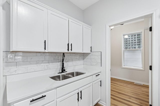 kitchen featuring a sink, white cabinets, light wood finished floors, decorative backsplash, and baseboards