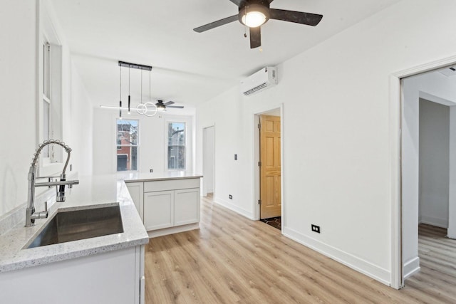 kitchen with light wood-style flooring, a ceiling fan, a wall unit AC, and a sink