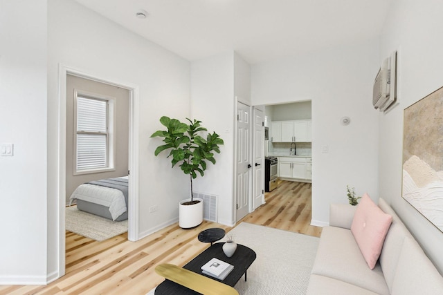 living area featuring light wood-style floors, visible vents, a wall mounted air conditioner, and baseboards