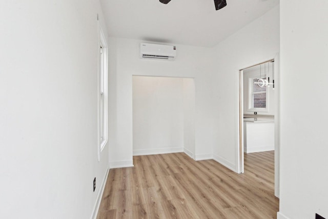 empty room with an AC wall unit, light wood-style floors, baseboards, and ceiling fan