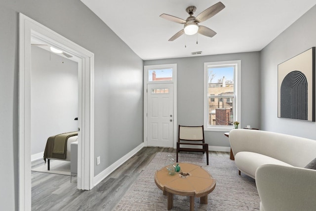 living area with baseboards, wood finished floors, visible vents, and ceiling fan