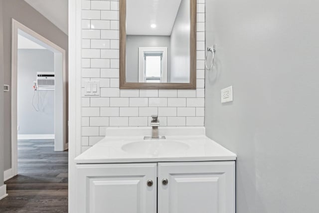 bathroom with baseboards, a wall unit AC, decorative backsplash, wood finished floors, and vanity