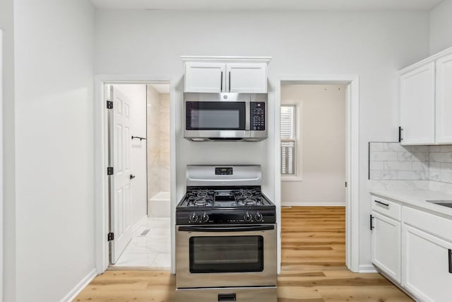 kitchen featuring light wood-type flooring, tasteful backsplash, white cabinetry, stainless steel appliances, and baseboards