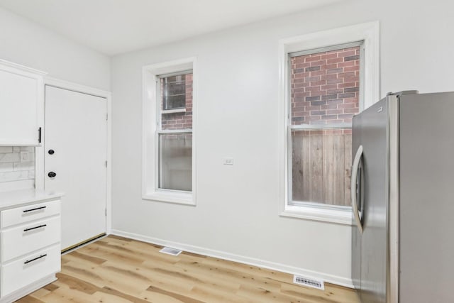 kitchen with white cabinets, light wood-style flooring, visible vents, and freestanding refrigerator