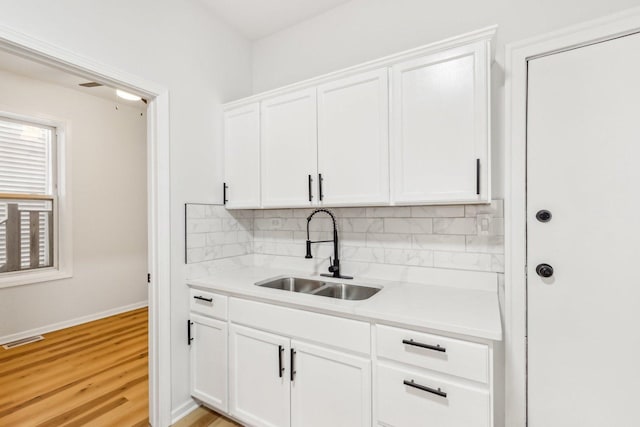 kitchen featuring visible vents, a sink, decorative backsplash, light countertops, and white cabinets