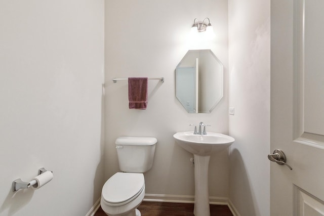 half bath with a sink, baseboards, toilet, and wood finished floors