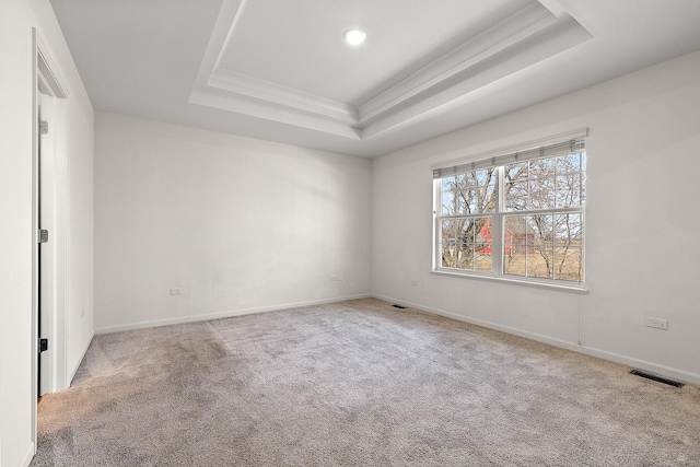 carpeted spare room featuring a raised ceiling, baseboards, visible vents, and ornamental molding