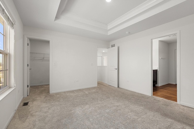 unfurnished bedroom featuring a tray ceiling, carpet floors, multiple windows, and visible vents