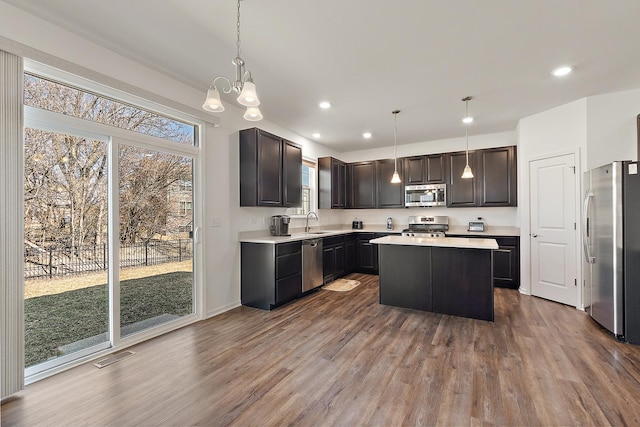 kitchen with wood finished floors, visible vents, a kitchen island, a sink, and stainless steel appliances