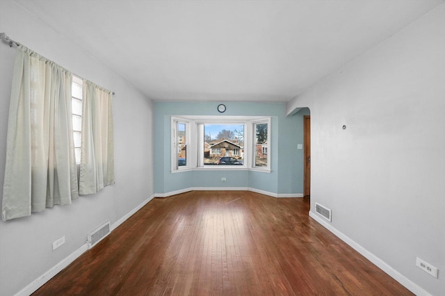 spare room featuring visible vents, baseboards, arched walkways, and wood finished floors