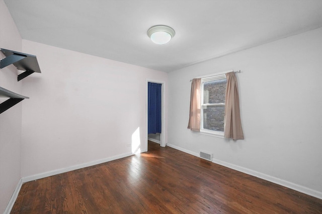 empty room with wood finished floors, visible vents, and baseboards