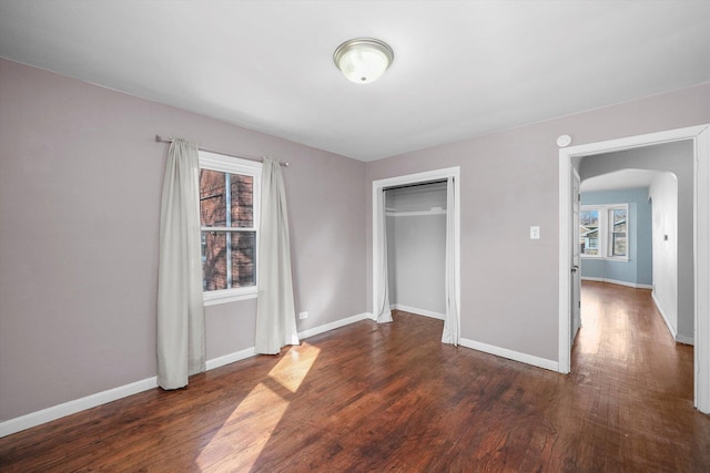 unfurnished bedroom with a closet, baseboards, arched walkways, and wood finished floors