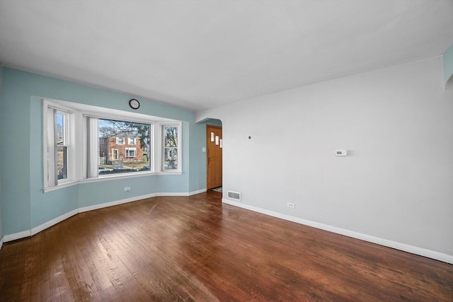 unfurnished room featuring visible vents, arched walkways, baseboards, and wood-type flooring